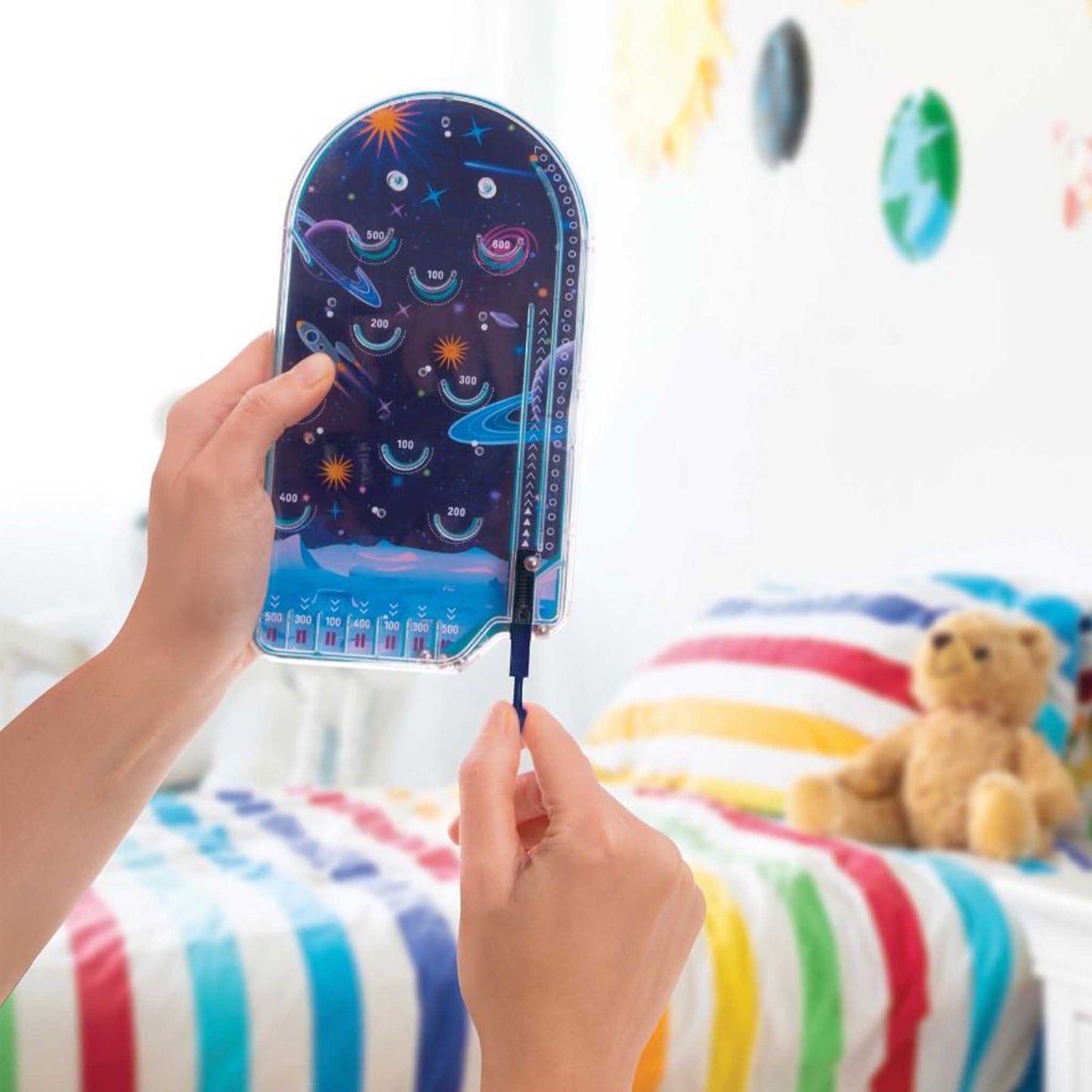 Hand holding a star chart with a teddy bear and colorful bedding in the background
