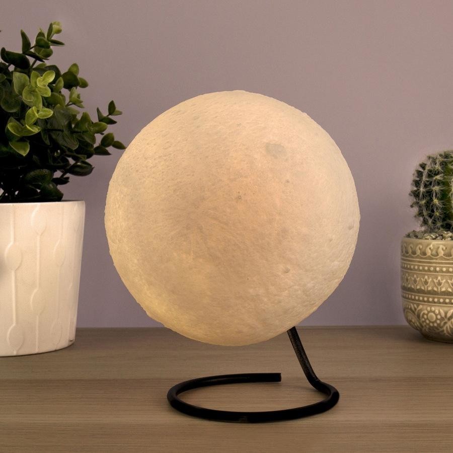 Moon lamp on a stand with a plant and decorative pot in the background