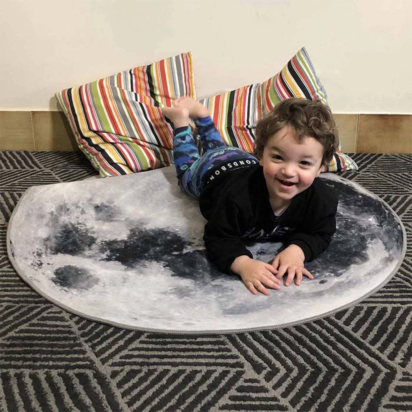 Child lying on a moon-shaped rug with colorful striped pillows in the background