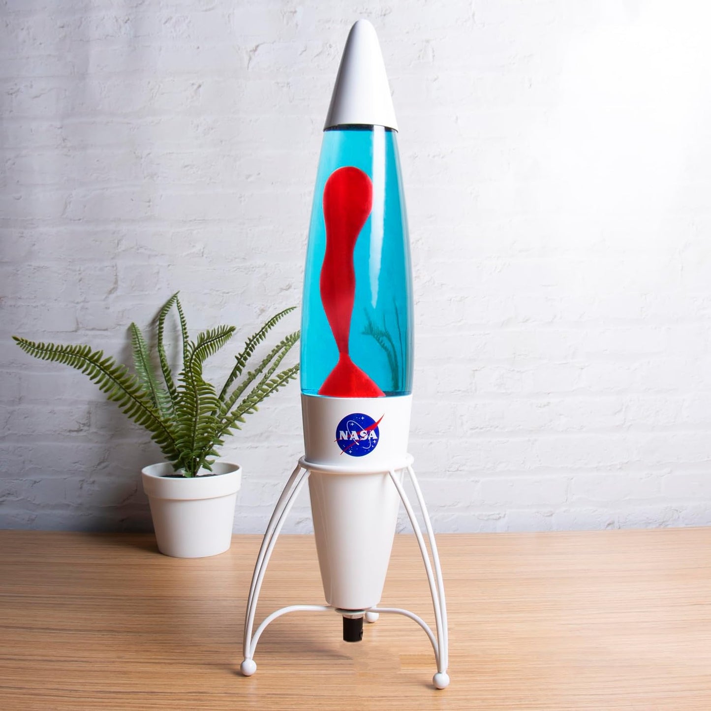 Lava lamp with NASA logo on a wooden surface with a plant in the background