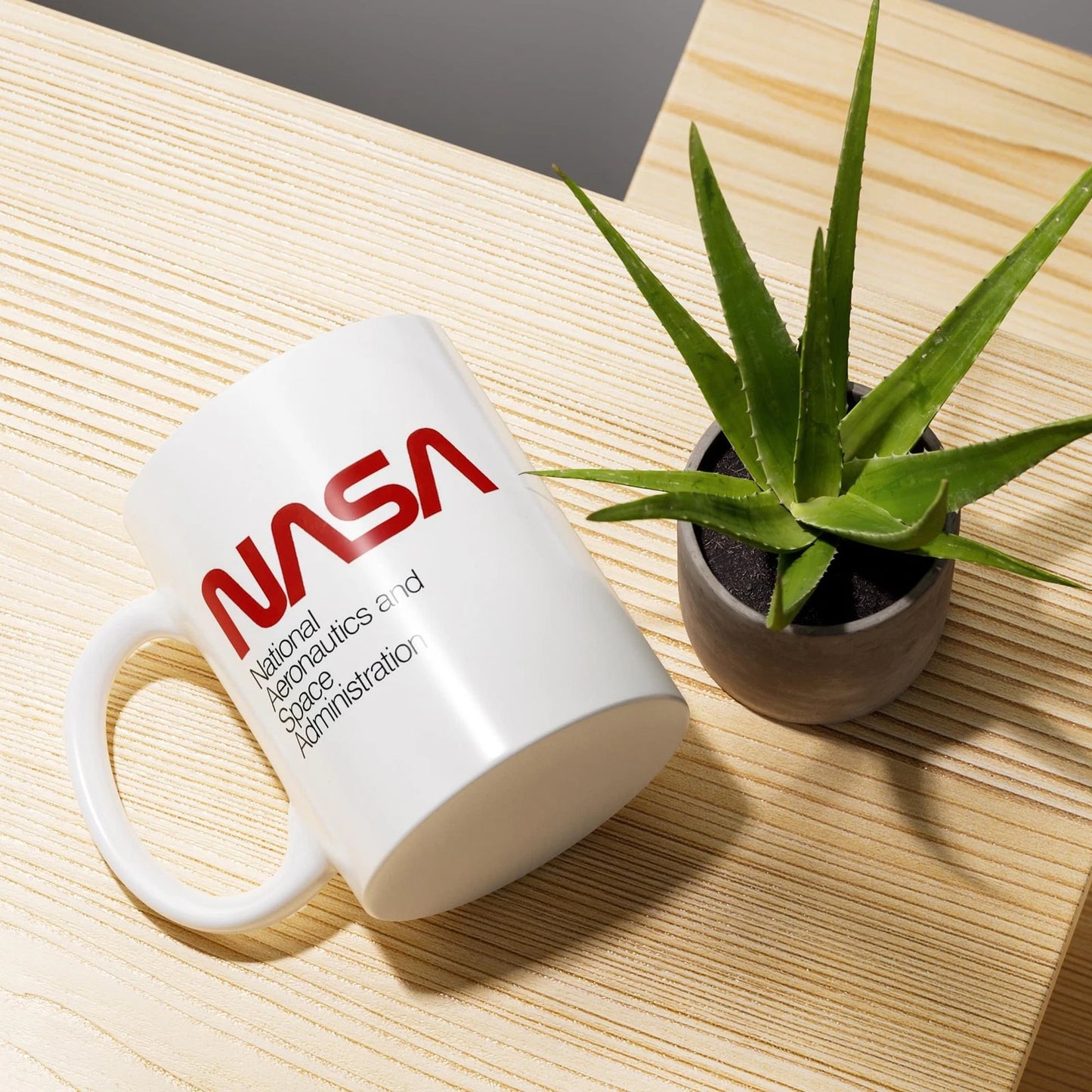 White mug with NASA logo on a wooden surface with a plant