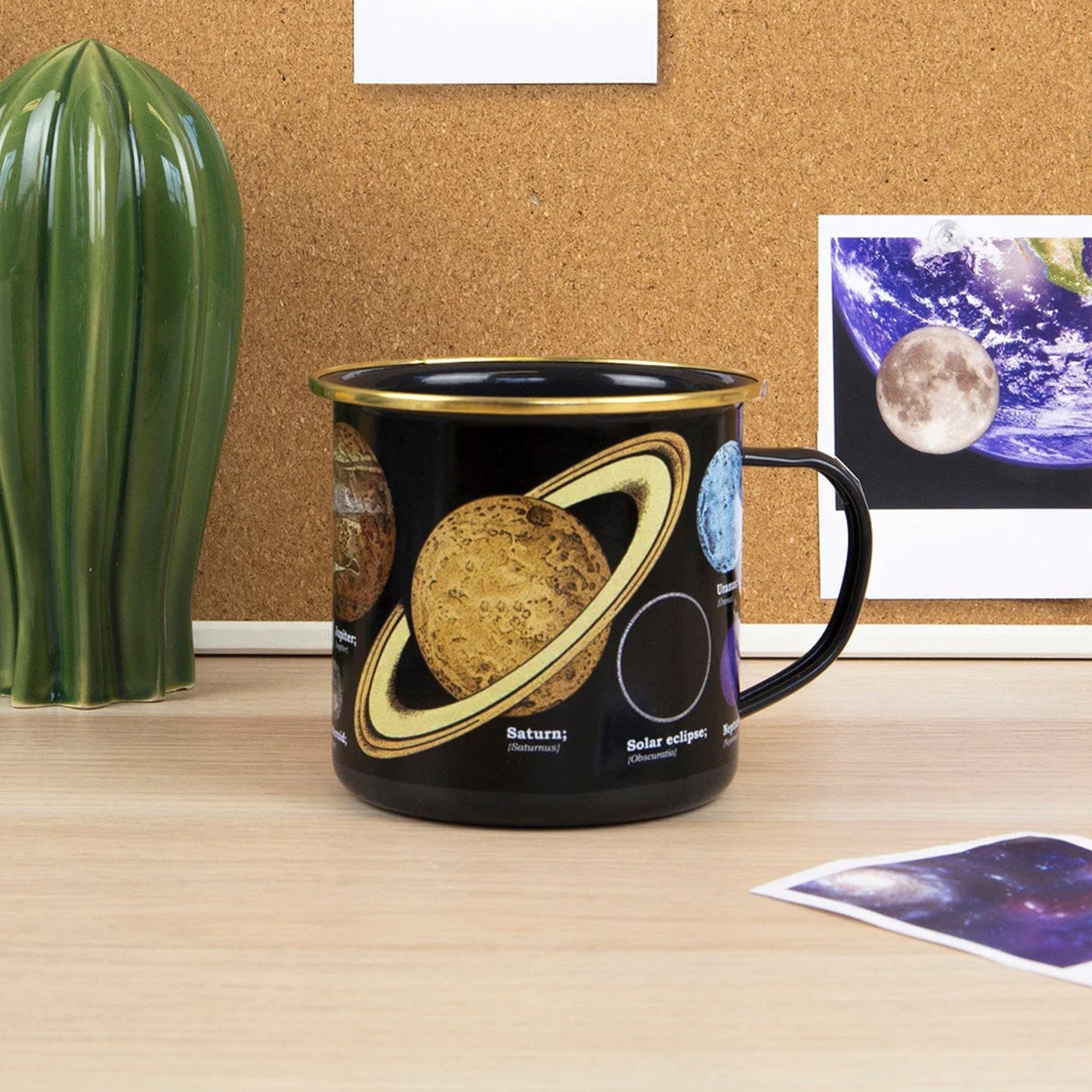Black mug with space-themed design on a desk next to a cactus plant