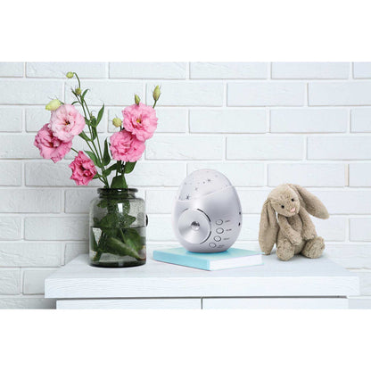 Baby monitor with pink flowers and a plush toy on a white surface against a light brick wall.