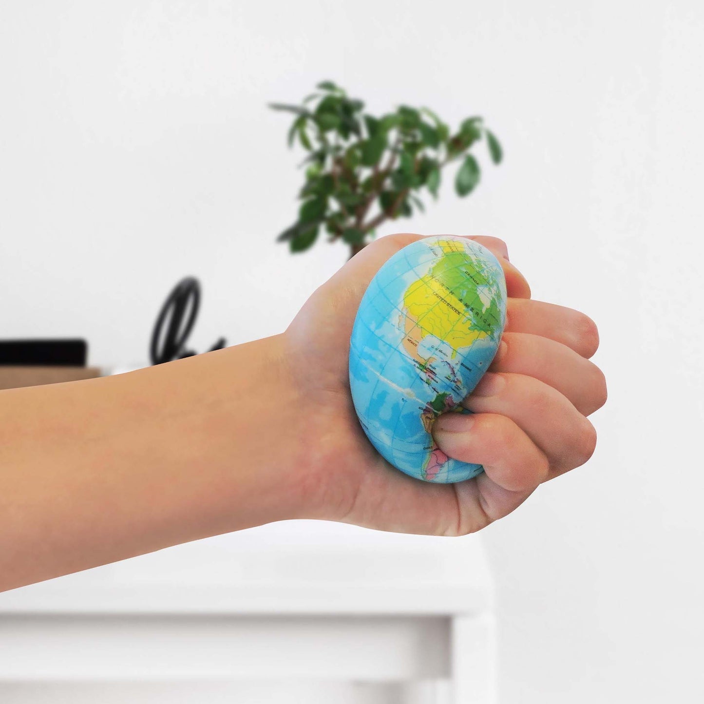 Hand holding a stress ball with a world map design against a blurred indoor background