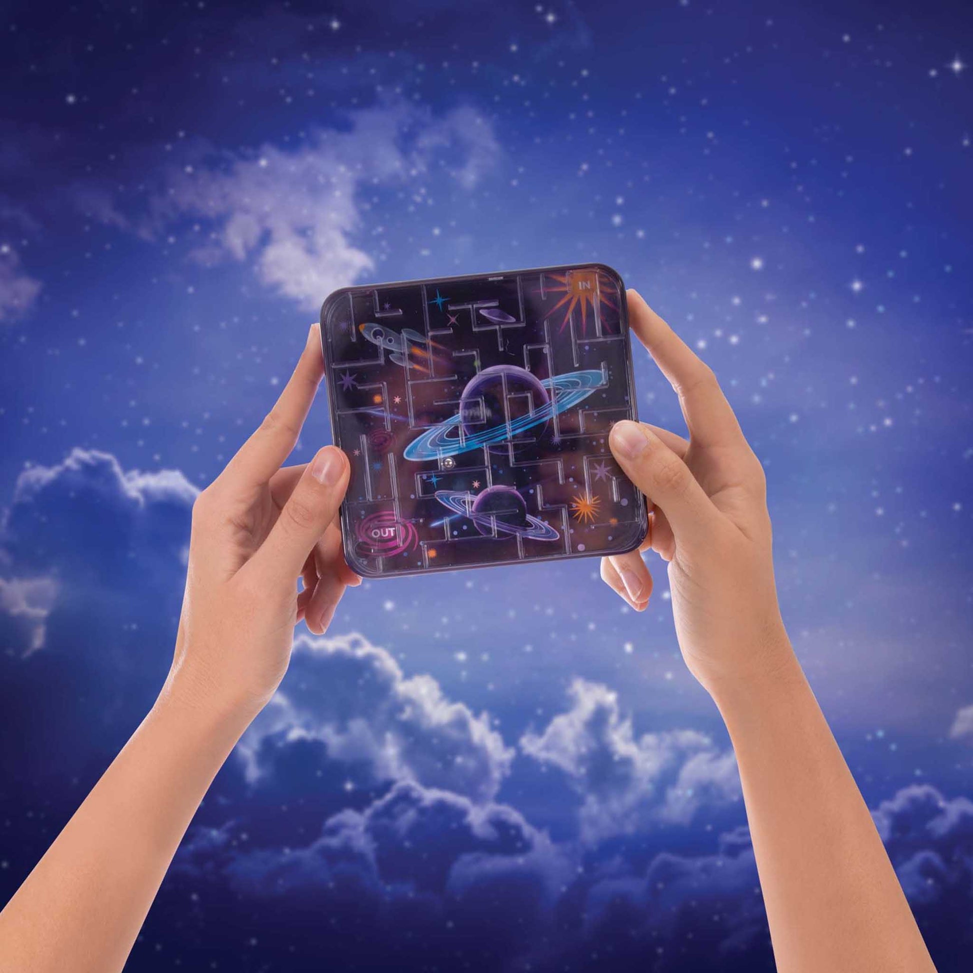 Hands holding a space themed maze toy against a night sky with clouds