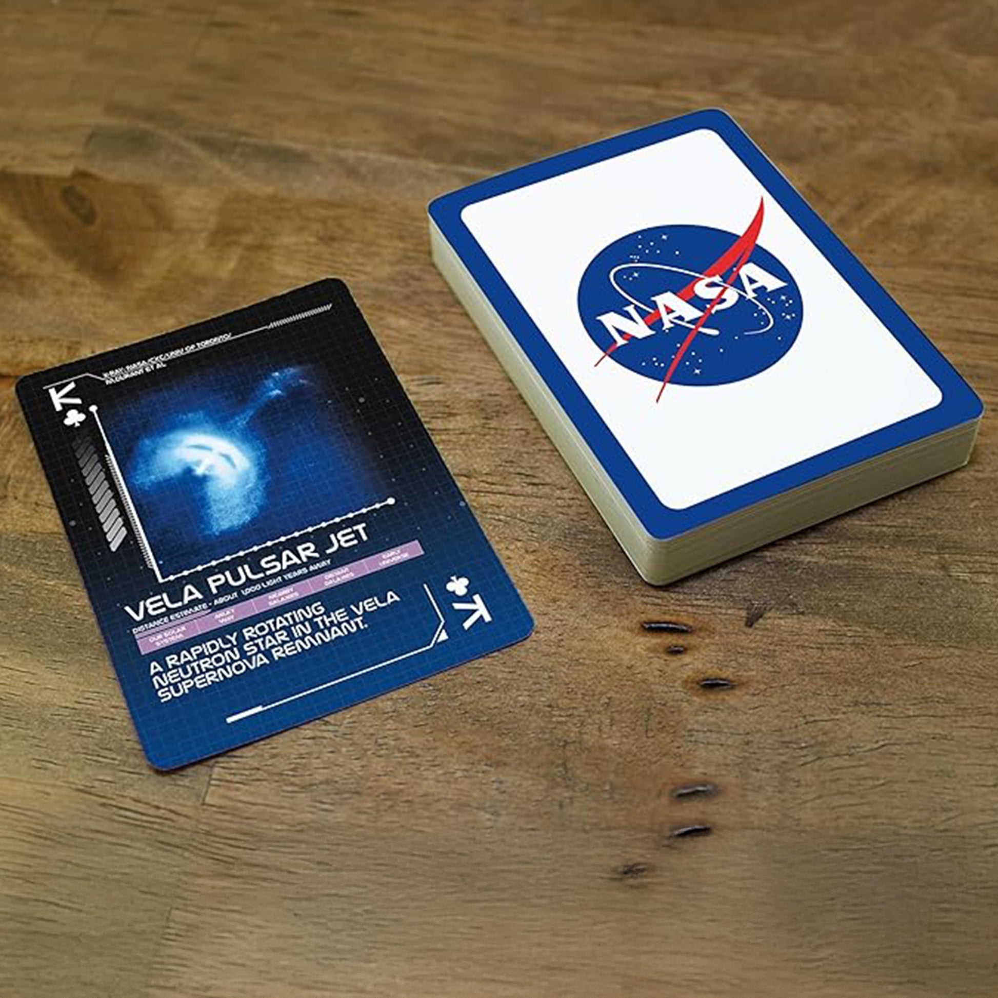 Two playing cards on a wooden surface, one with a blue card featuring a space image and text, the other with NASA logo.