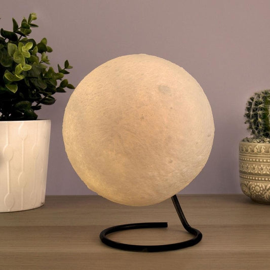 Moon lamp on a stand with a plant and decorative pot in the background