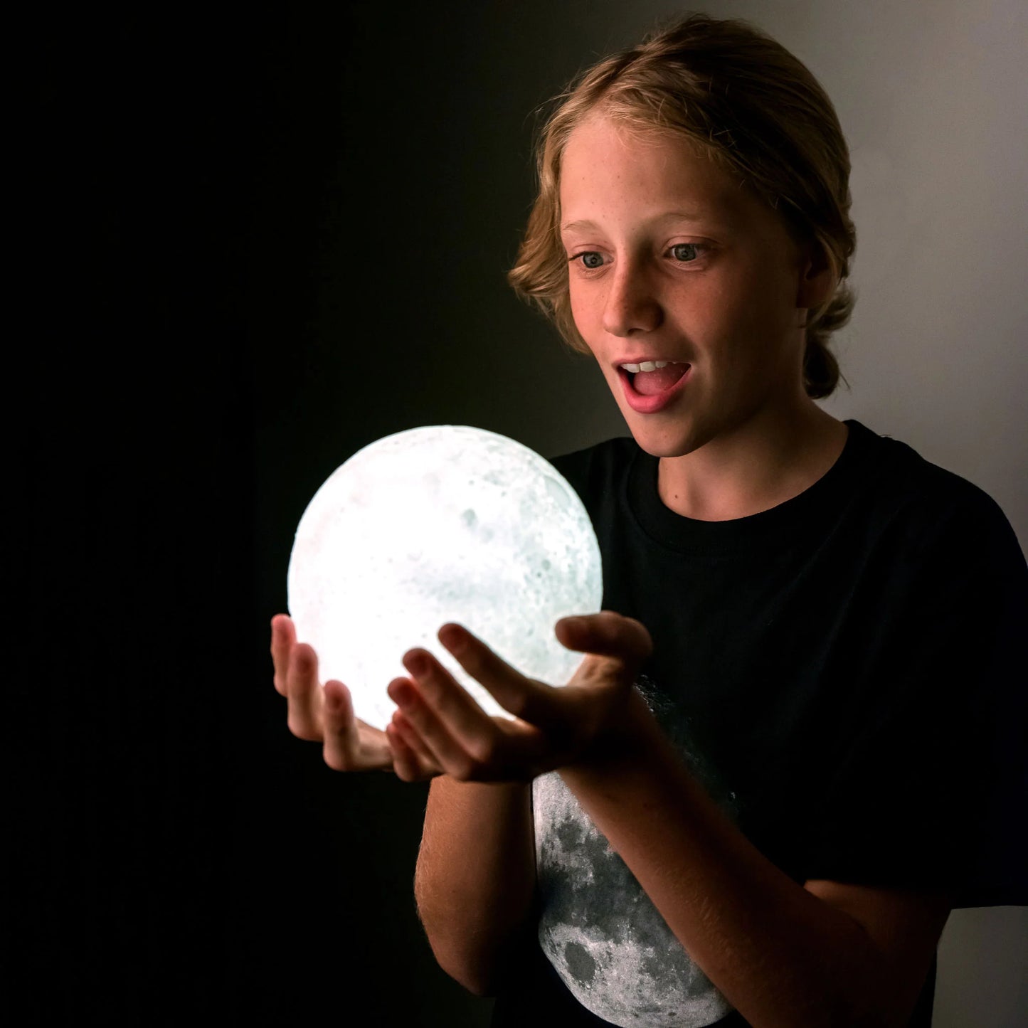 Person holding a moon-shaped light in a dark setting