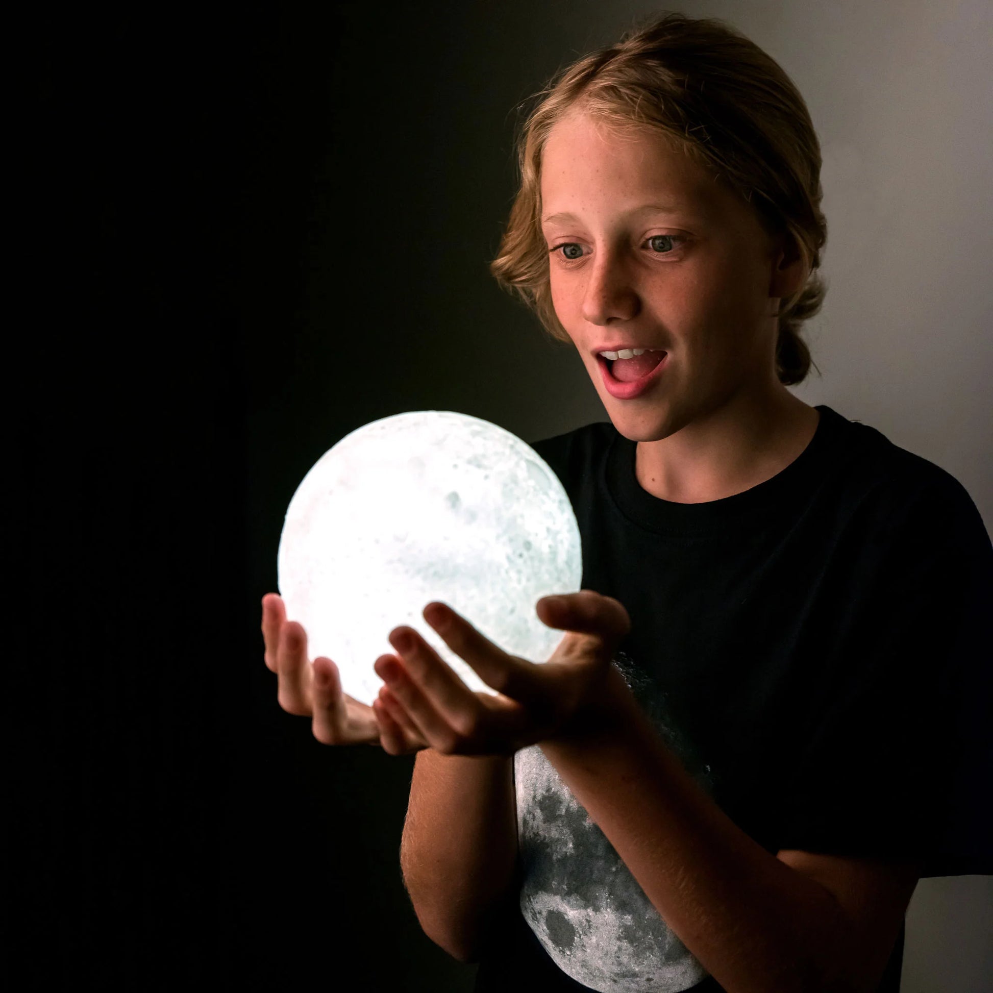 Person holding a moon-shaped light in a dark setting