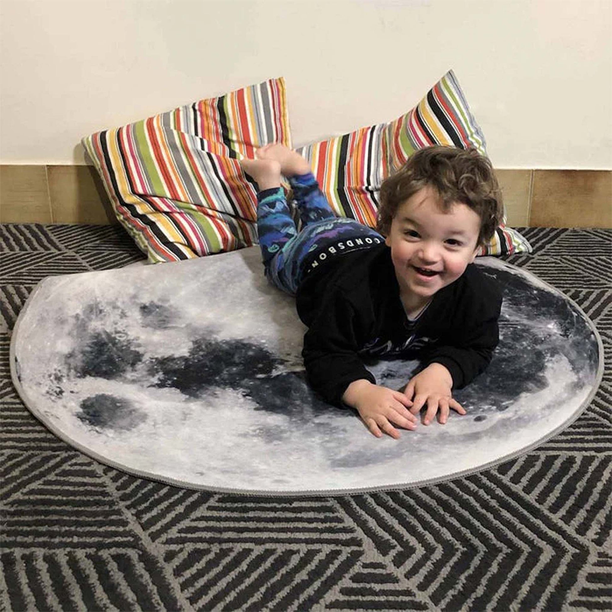Child lying on a moon-shaped rug with colorful striped pillows in the background