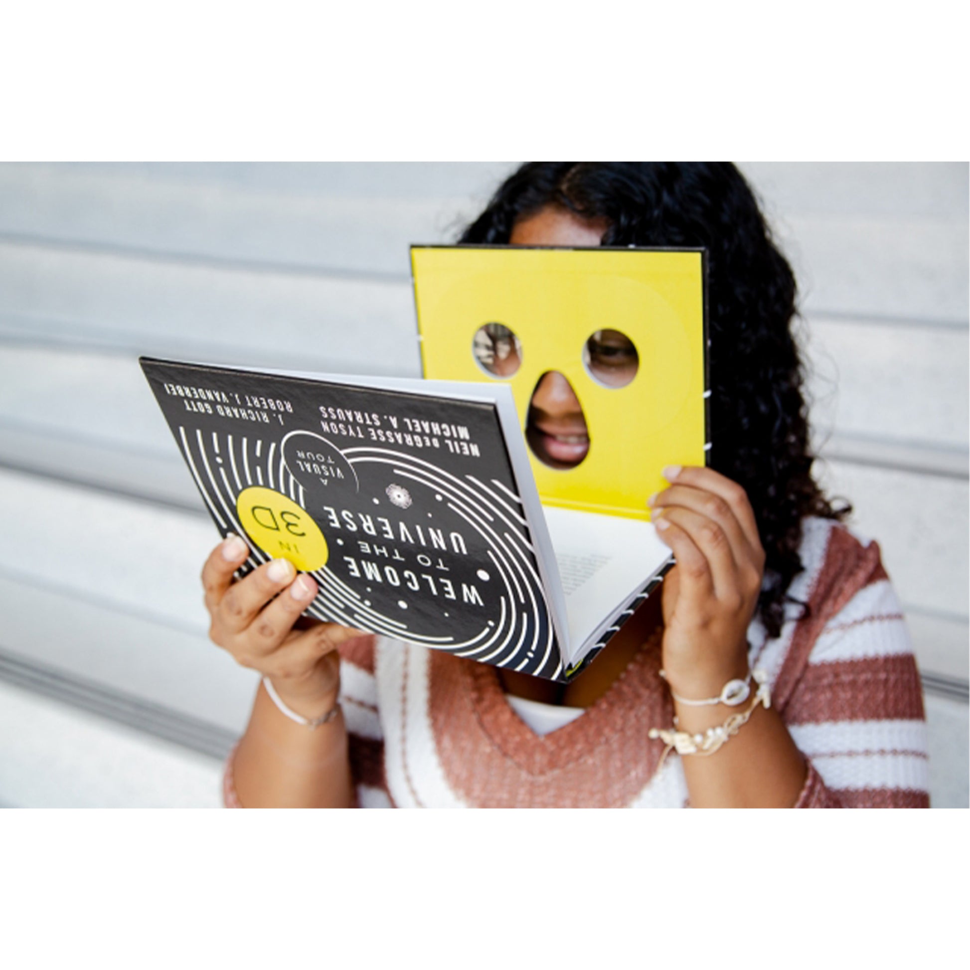 Person holding a book with a yellow mask over their face