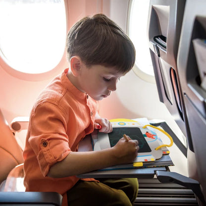 Child sitting in an airplane seat, drawing on a tablet.